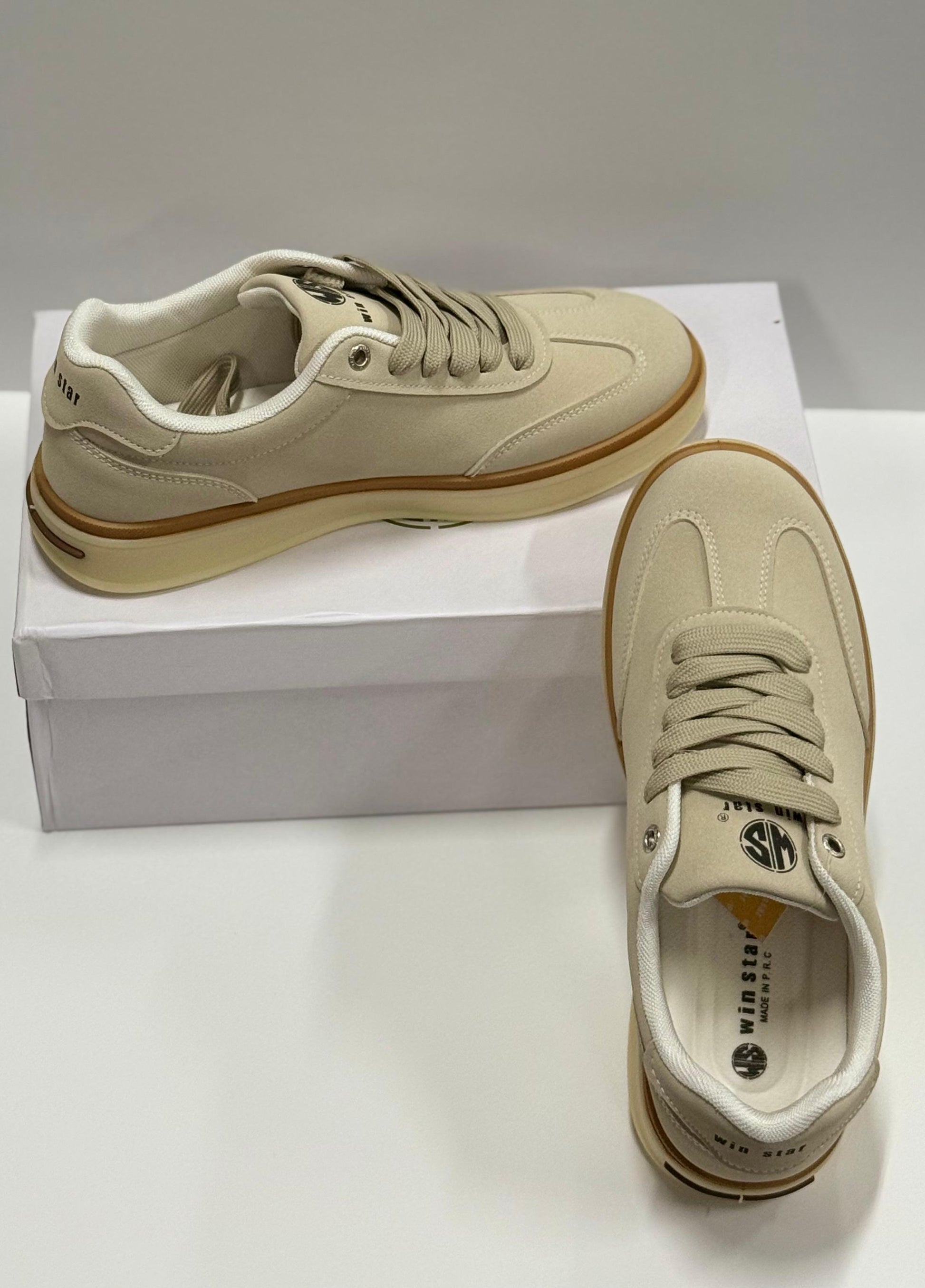 Pair of beige sneakers with brown soles on a white box against a white background