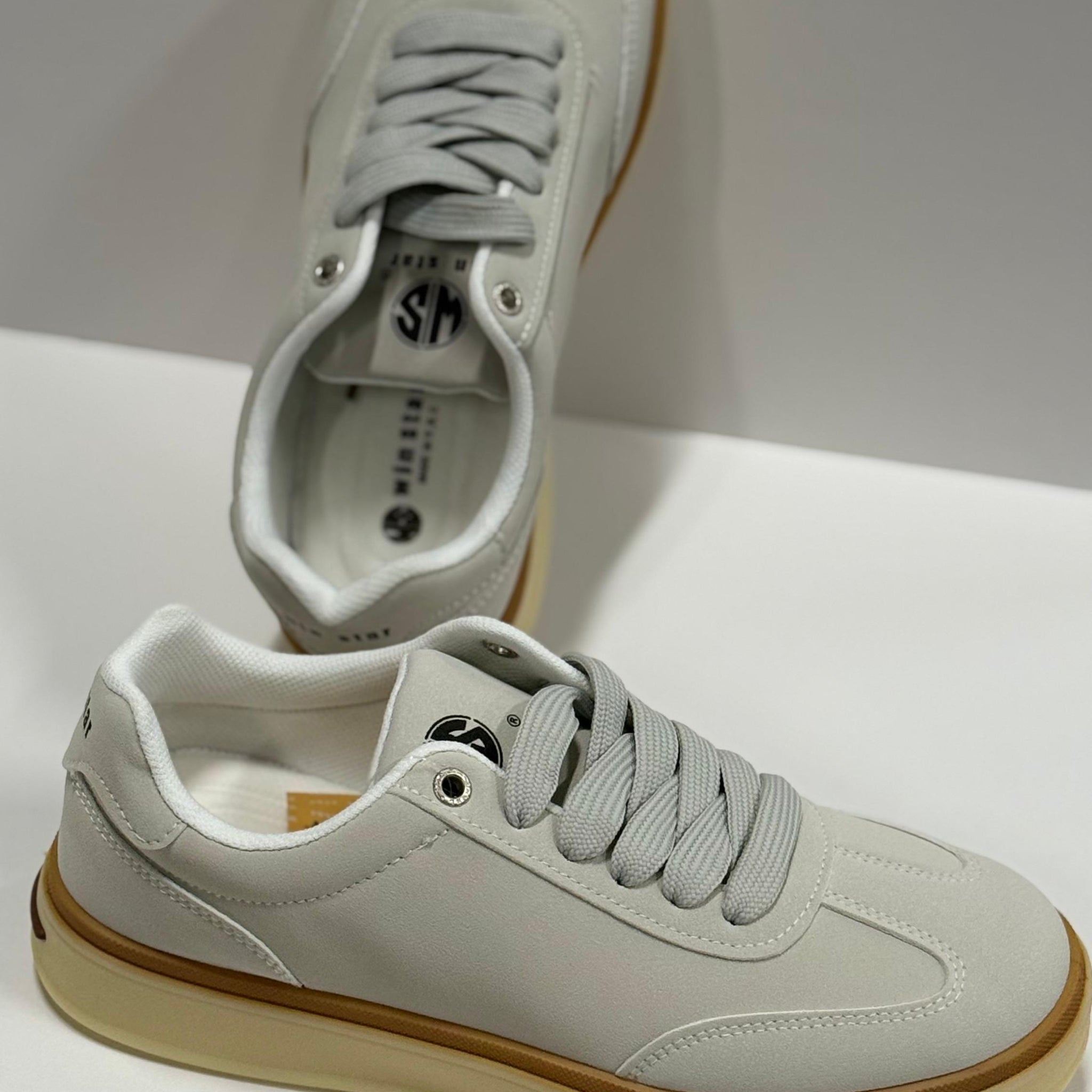 Pair of light gray sneakers with brown soles on a white background