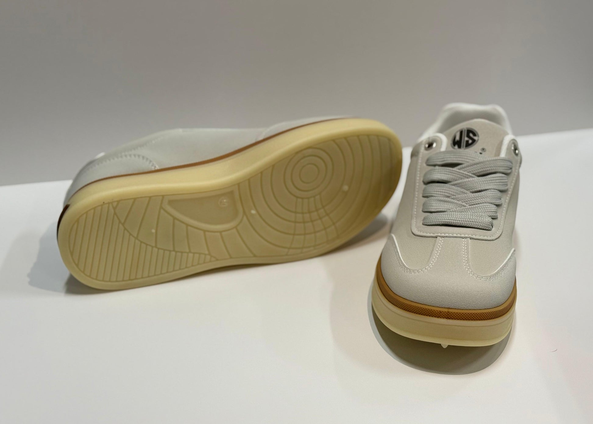 White sneakers with brown soles on a white surface