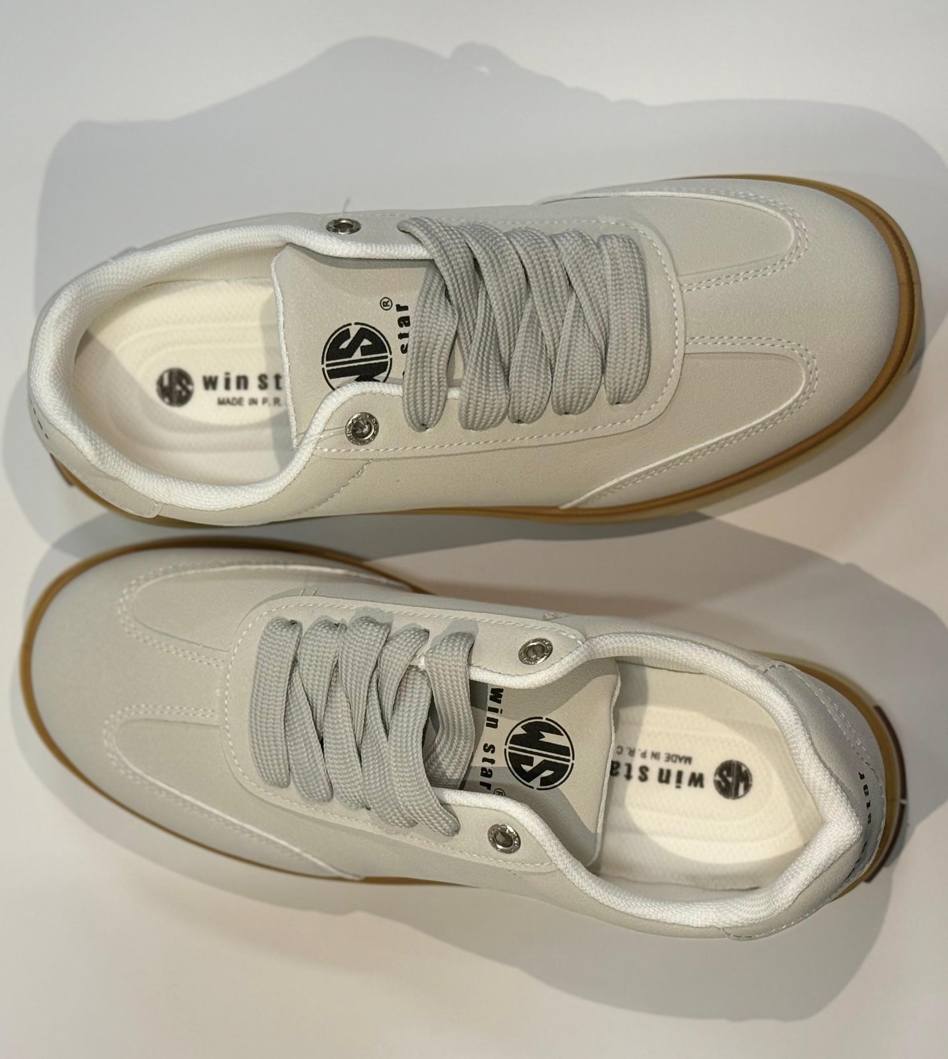 Pair of white sneakers with brown soles on a light gray background